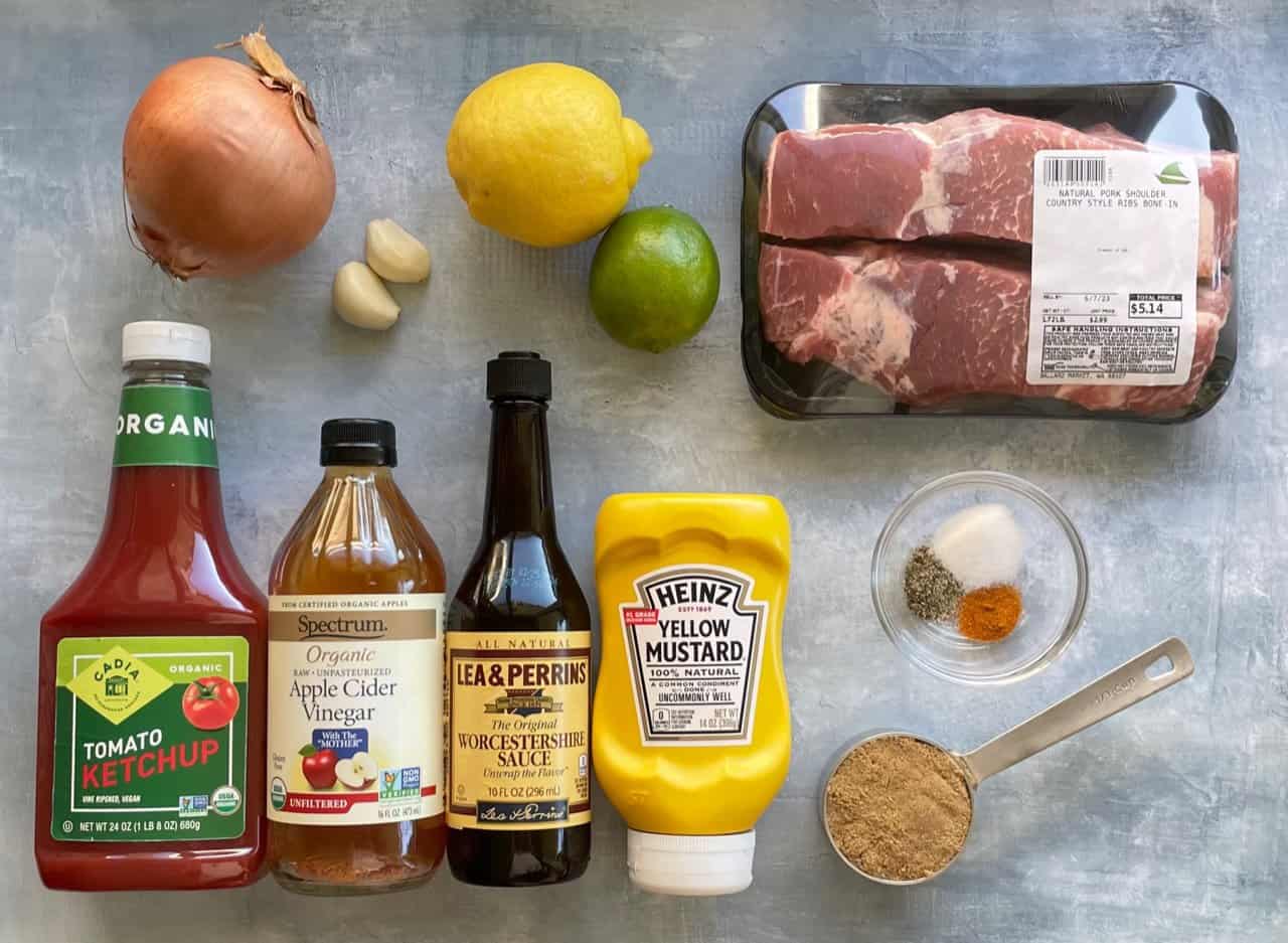Country style pork ribs, brown sugar, paprika, garlic powder, onion powder, salt, pepper, barbecue sauce, apple cider vinegar, and broth arranged on a kitchen counter