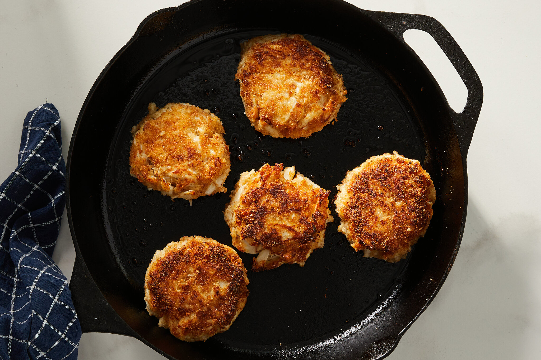 Crab cakes browning in a cast iron skillet with a thin sheen of oil on a stovetop