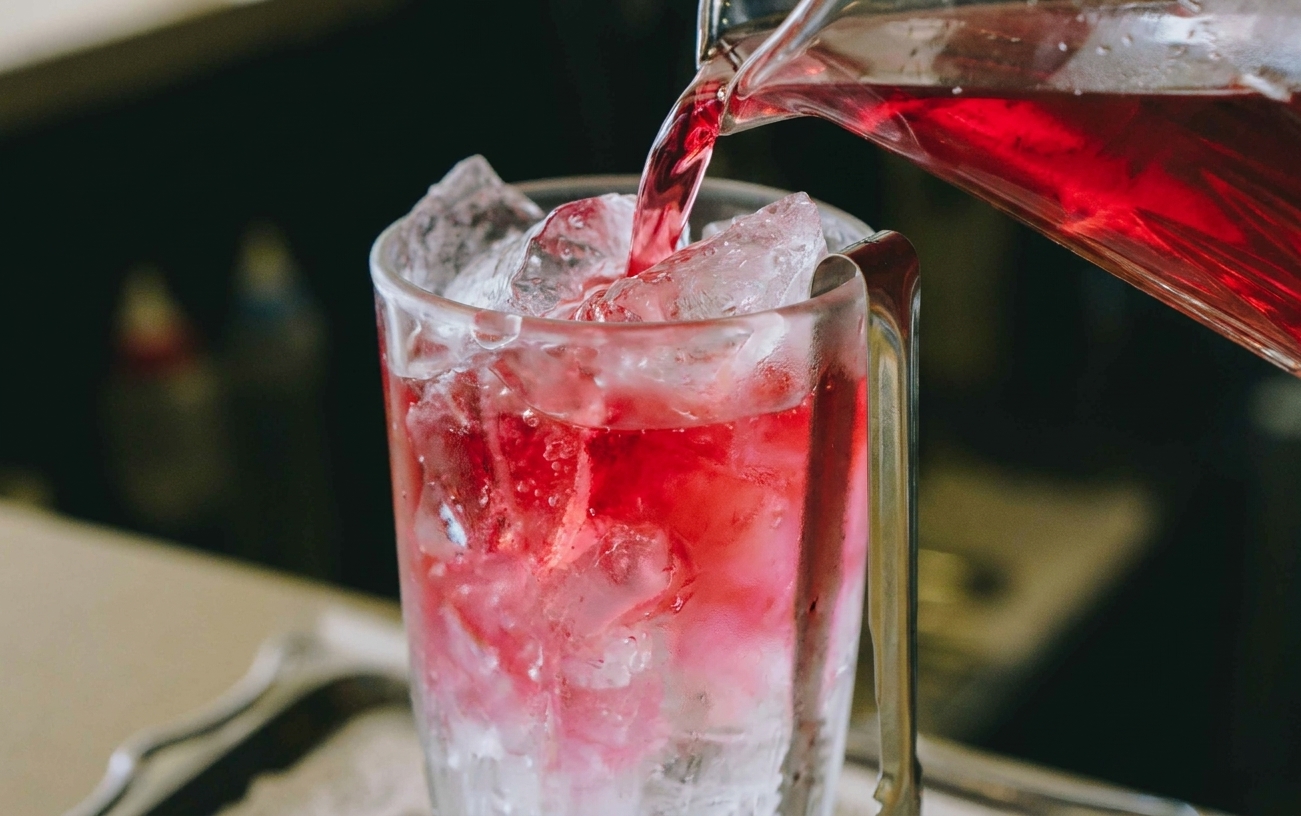 Cranberry juice being poured into an ice filled glass, turning the drink bright pink
