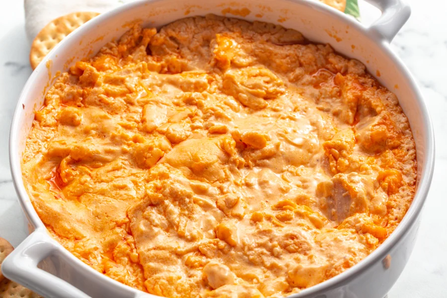 Cream cheese, buffalo wing sauce, shredded chicken, shredded cheese, and seasonings laid out on a kitchen counter for making Buffalo chicken dip