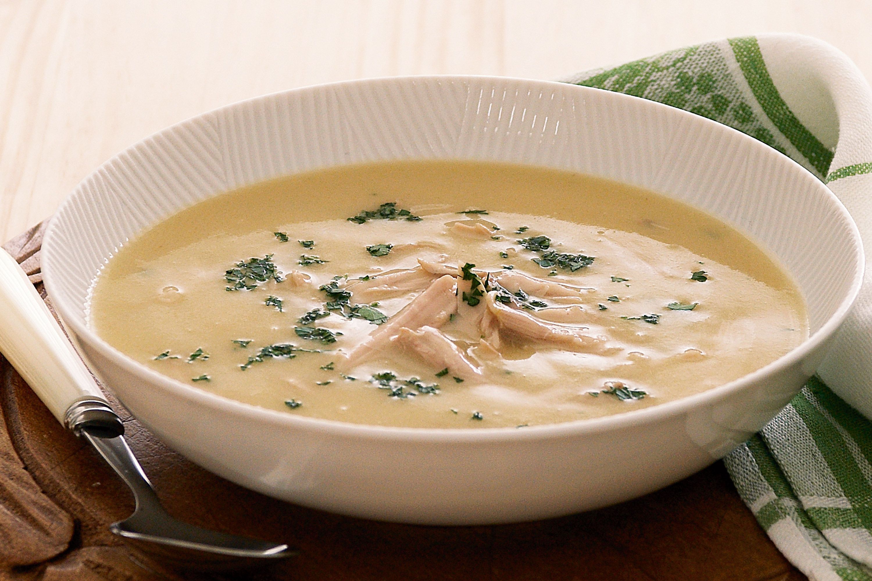 Cream of chicken soup cans, a bowl of chicken broth, and raw chicken breasts on a cutting board in a bright home kitchen