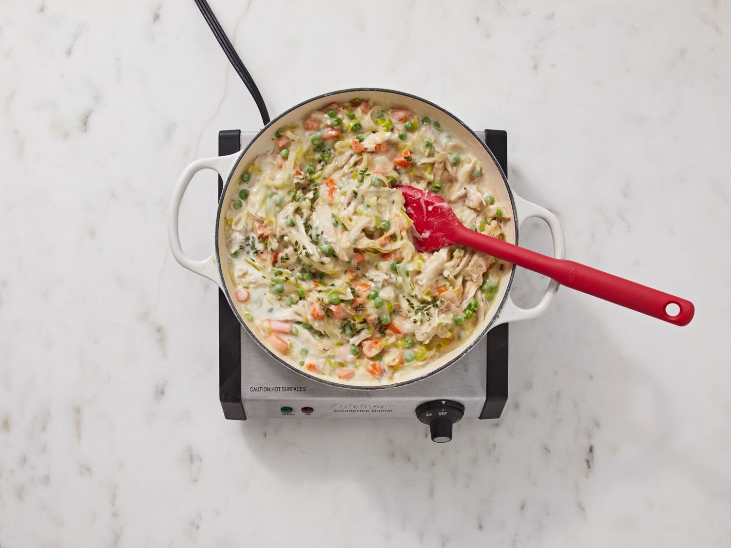 Creamy chicken pot pie filling simmering in a skillet with visible peas and carrots, a wooden spoon resting on the edge