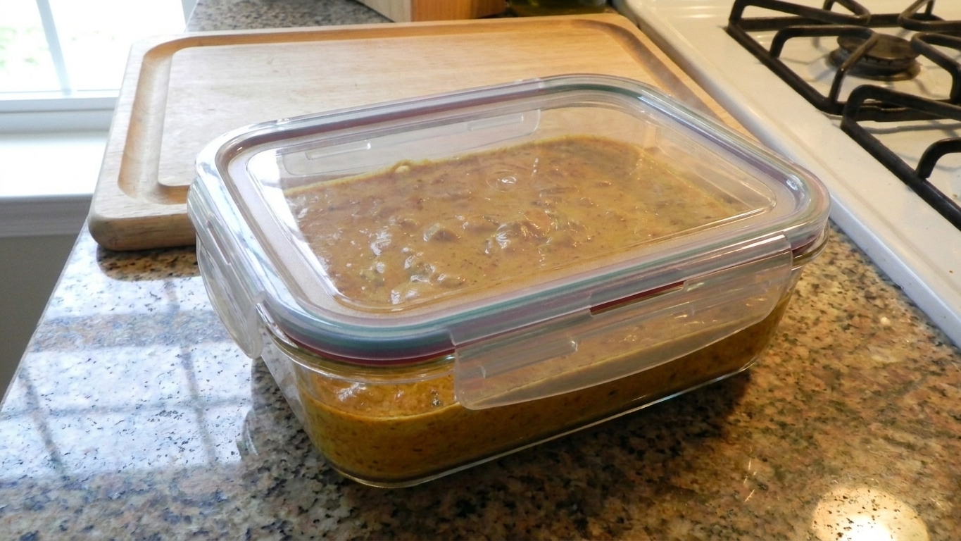 Creamy curry sauce in a clear glass container with a tight lid on a kitchen counter, ready for storing in the fridge