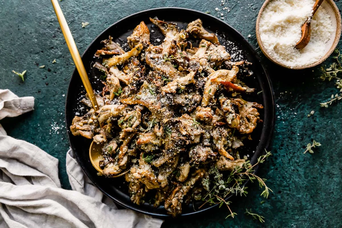 Cremini mushrooms, garlic, Parmesan, butter, lemon, parsley, and dry pasta arranged on a light stone kitchen counter, overhead photo