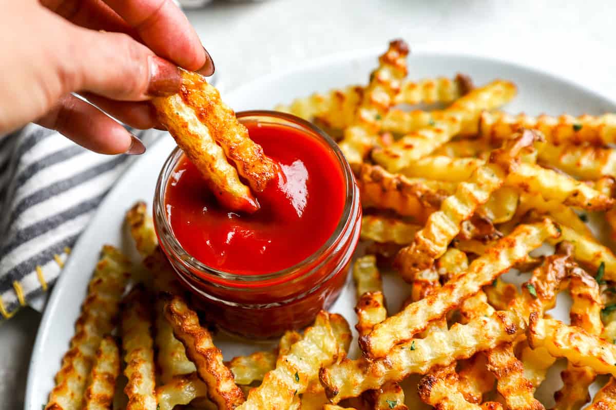 Crinkle-cut fries being dipped into a small ramekin of creamy Cane’s-style sauce on a wooden table