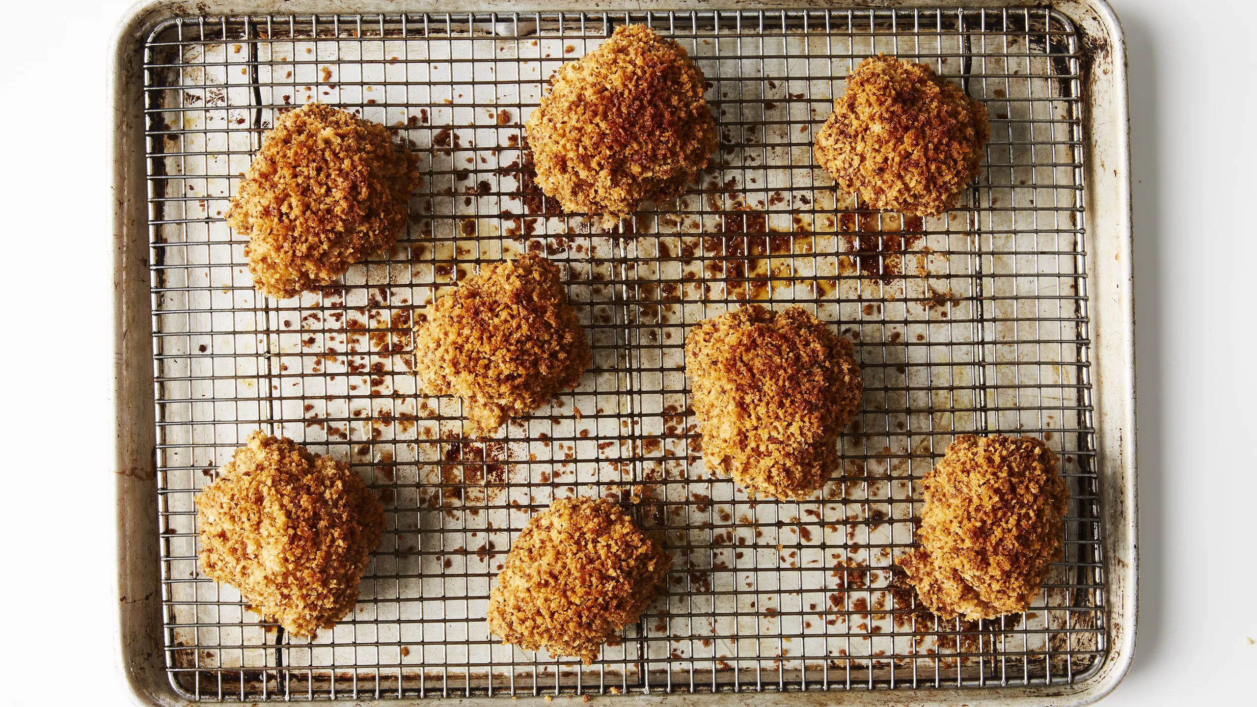 Crispy chicken cutlets resting on a wire rack set over a baking sheet on a kitchen counter to keep the coating crunchy