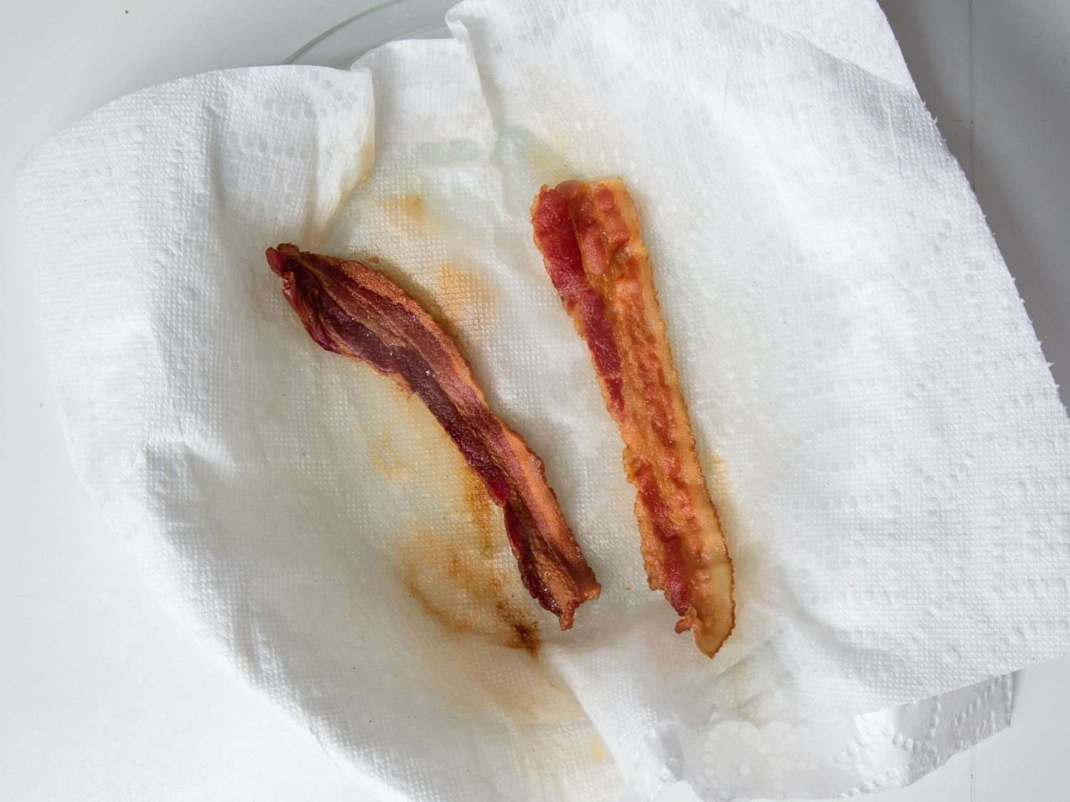 Crispy cooked bacon draining on paper towels on a plate beside a skillet on a home stovetop, warm kitchen lighting