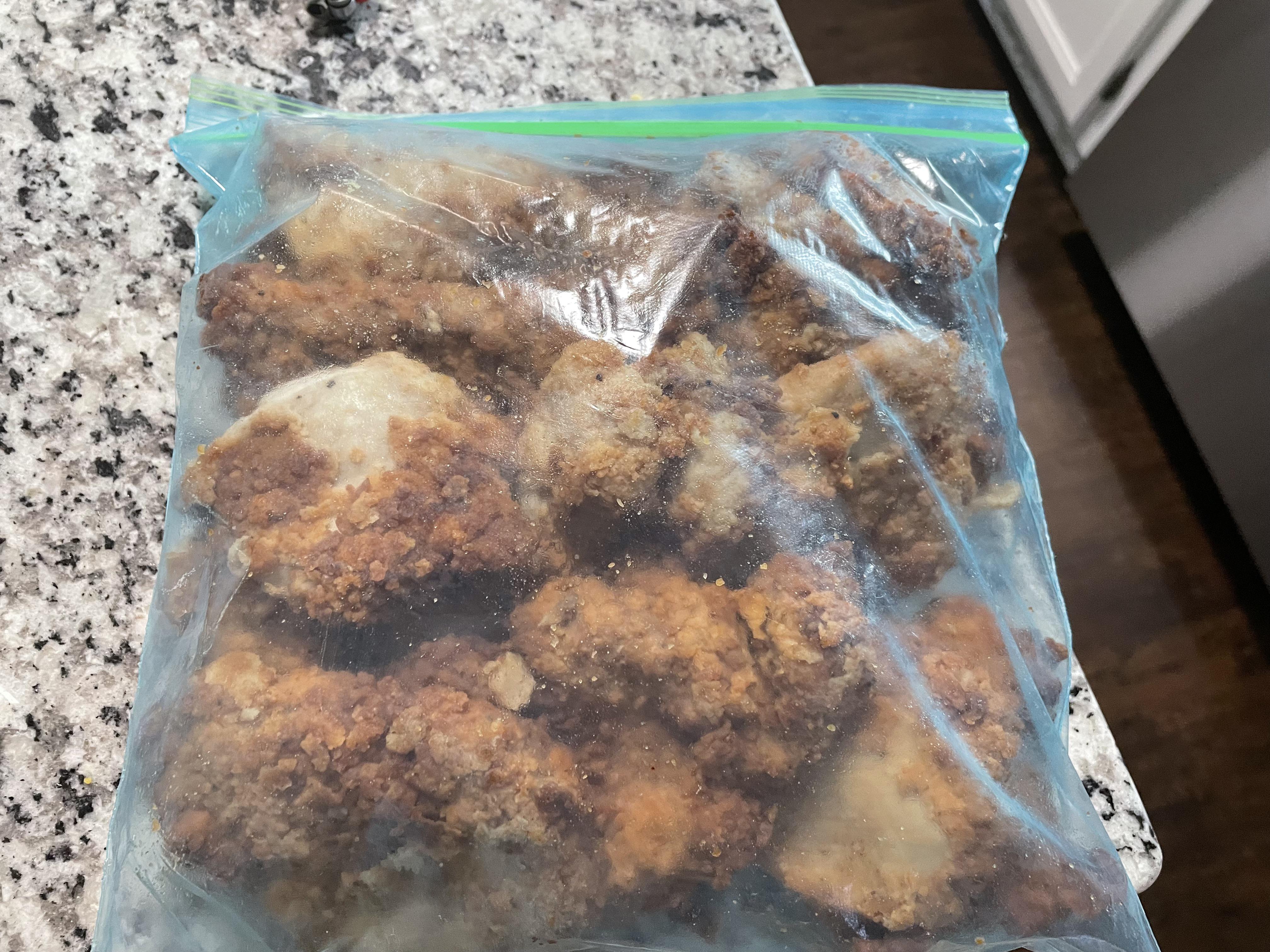 Crispy fried chicken pieces resting in a shallow airtight container lined with paper towel on a kitchen counter