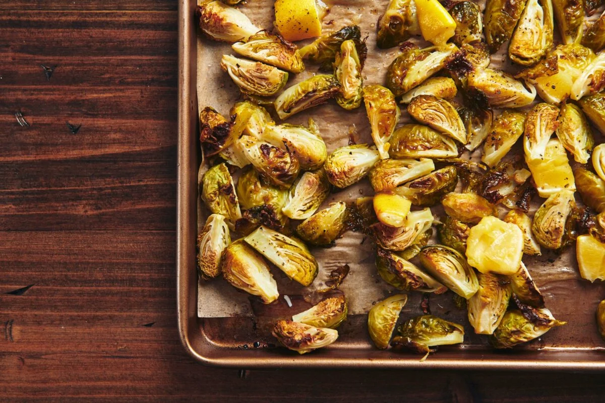 Crispy roasted Brussels sprouts on a serving platter with a lemon wedge and a small bowl of flaky salt on a dining table
