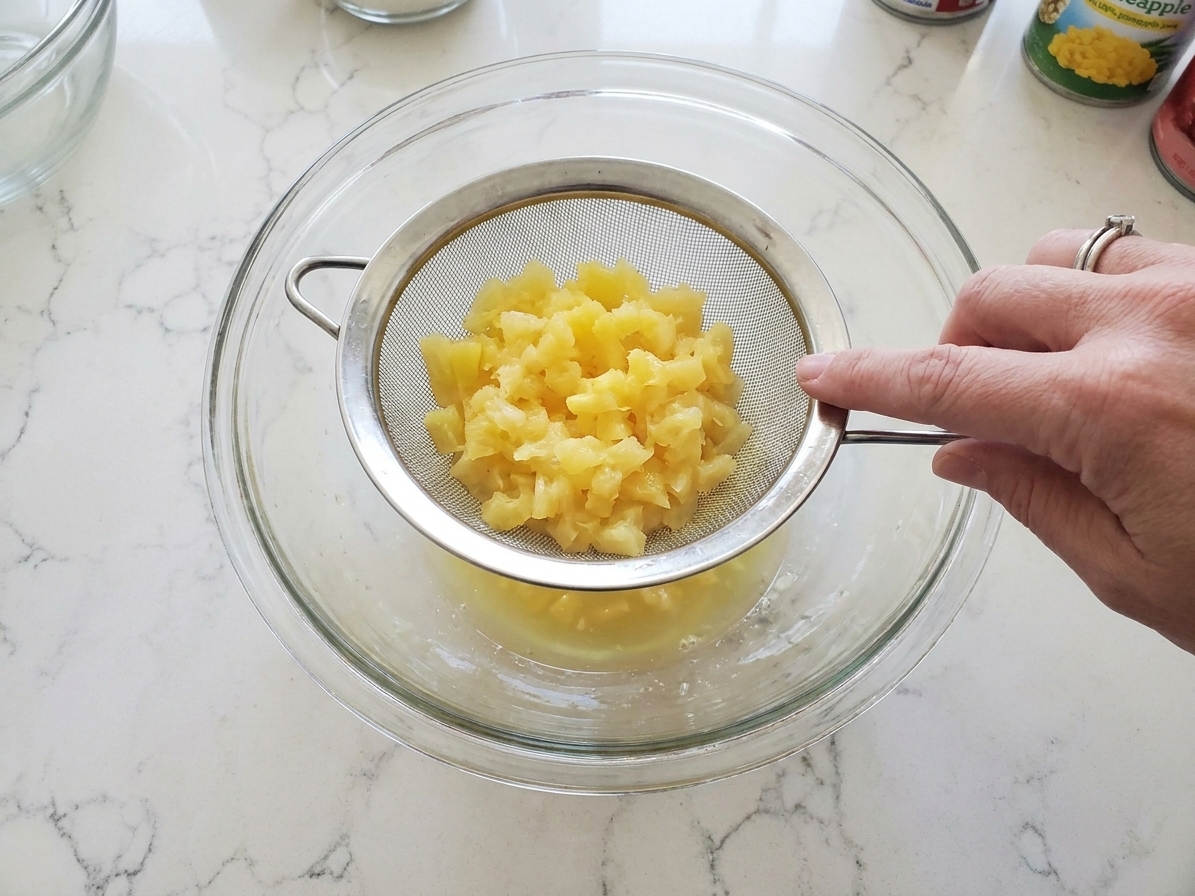 Crushed pineapple draining in a fine-mesh strainer over a bowl on a kitchen counter