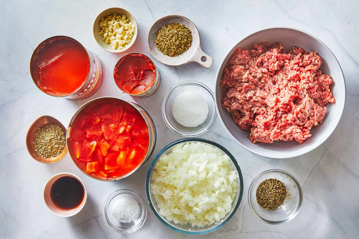 Crushed tomatoes, tomato paste, onion, garlic, olive oil, dried herbs, salt, and pepper arranged on a clean kitchen counter