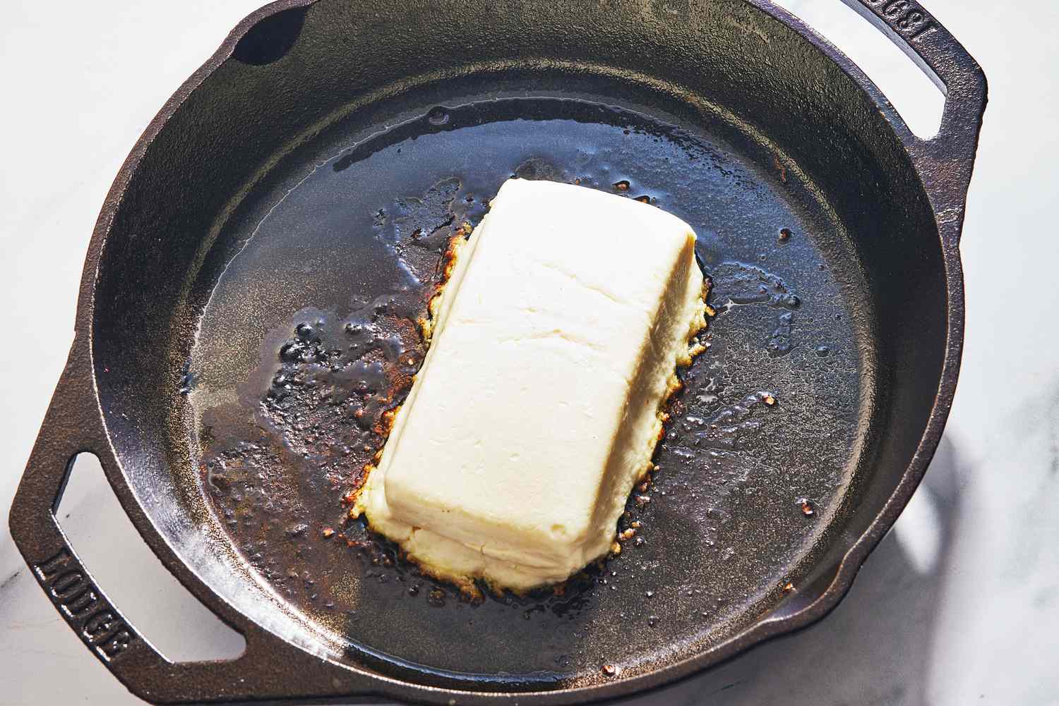 Cubed cream cheese melting into browned sausage in a skillet while being stirred with a wooden spoon on a stovetop