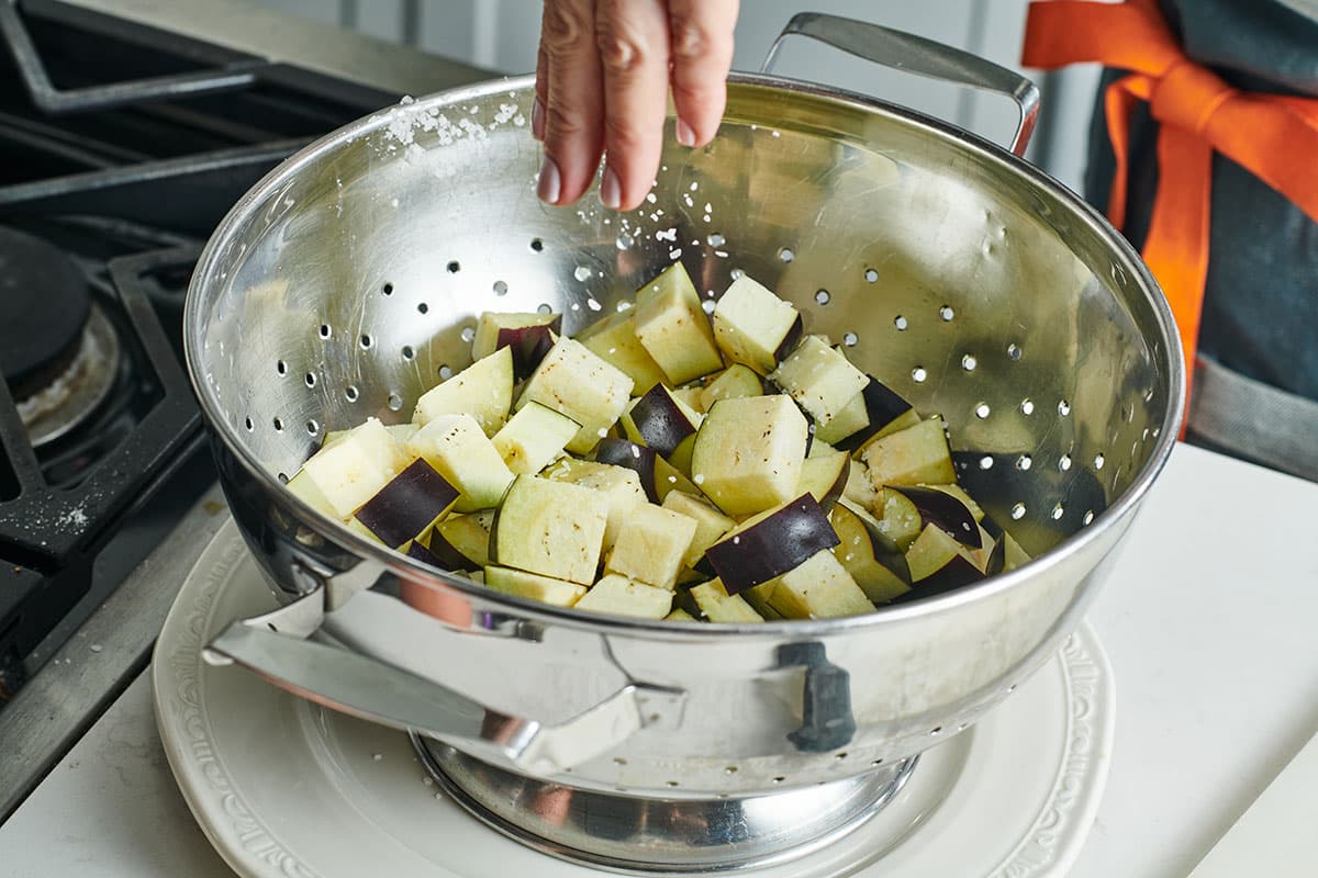 Cubed eggplant sprinkled with salt on a rimmed baking sheet lined with paper towels, ready to rest before cooking