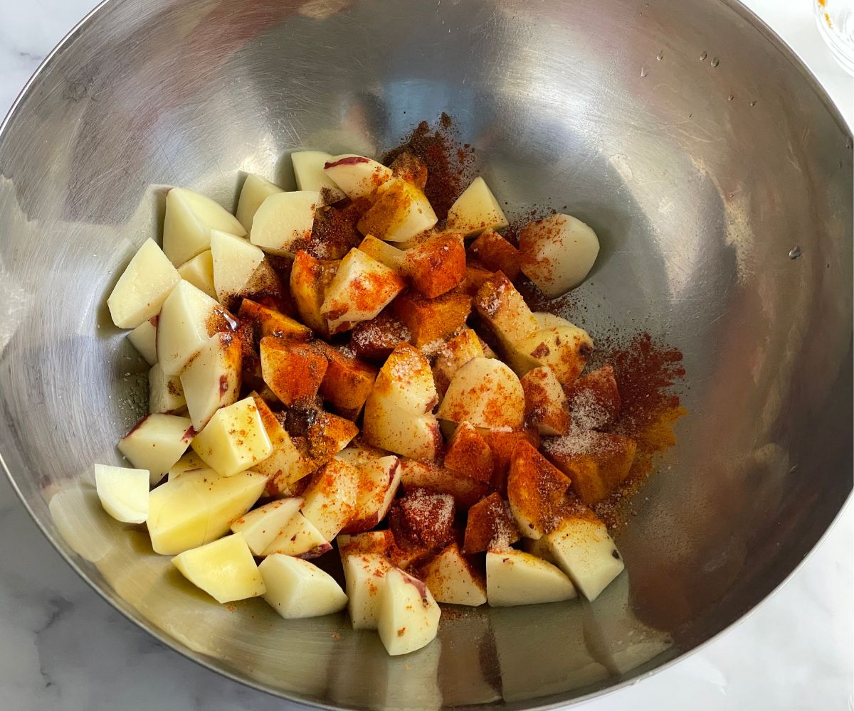Cubed potatoes in a mixing bowl with salt and pepper, ready to be fried on a bright kitchen counter