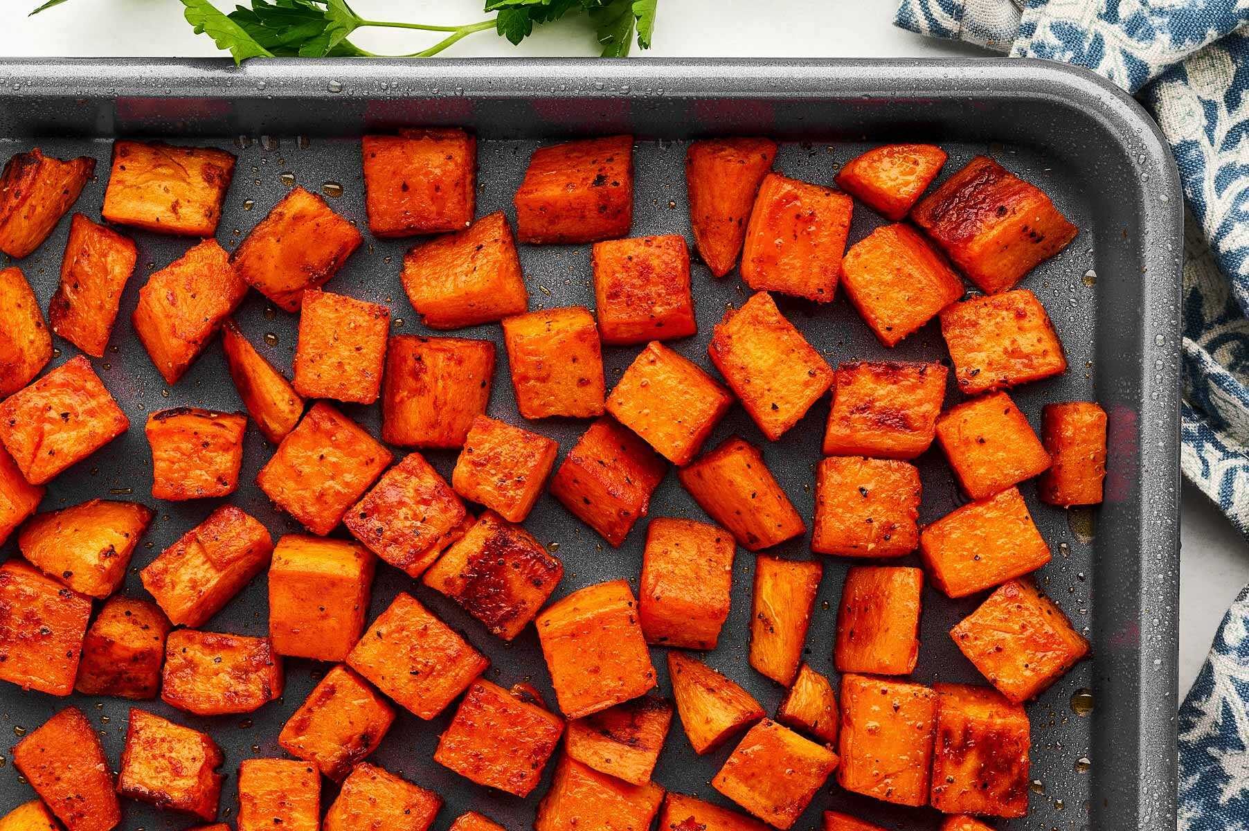 Cubed sweet potatoes tossed with spices and olive oil spread out on a parchment-lined sheet pan