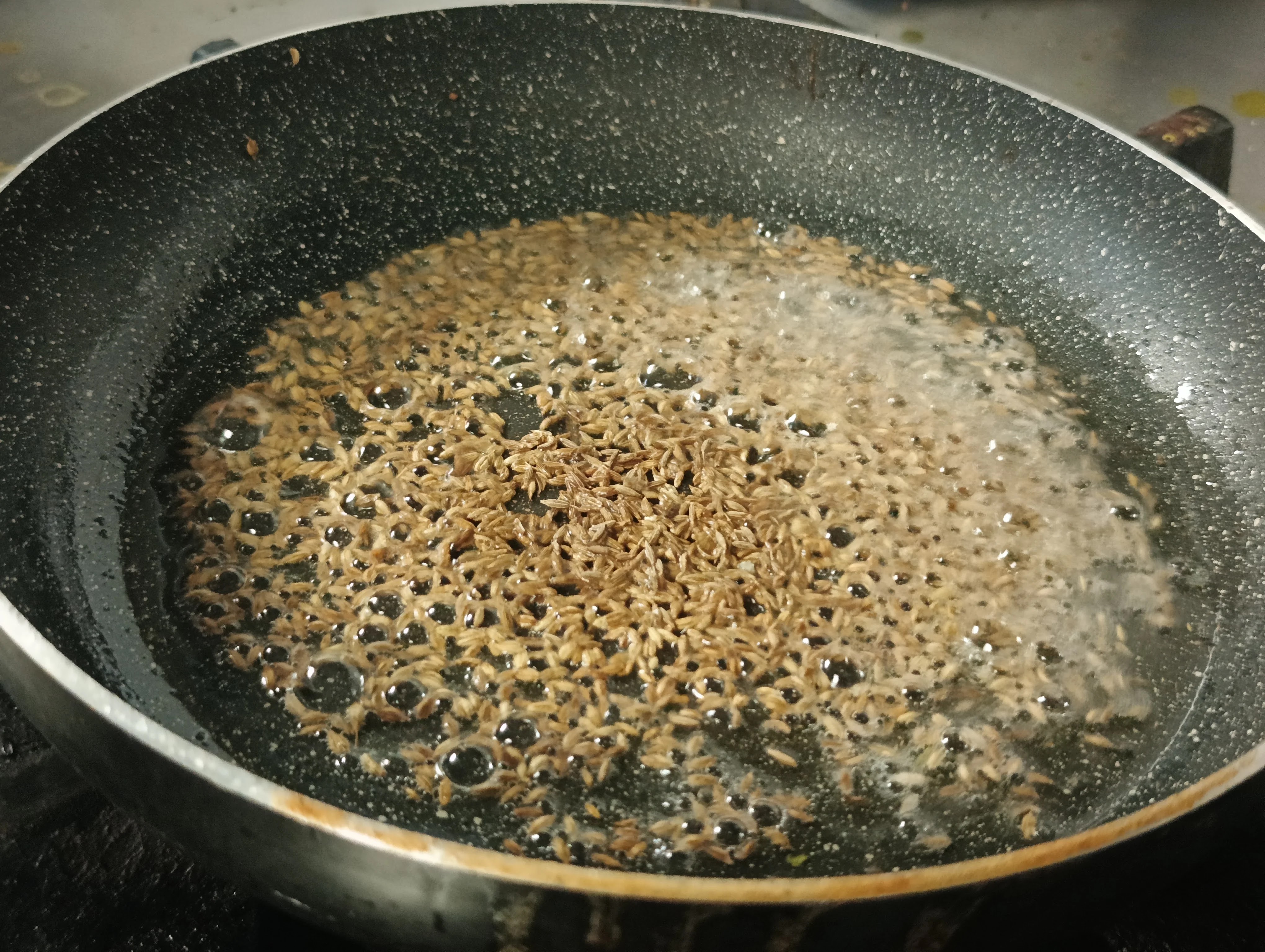 Cumin seeds sizzling in melted ghee with whole spices in a saucepan