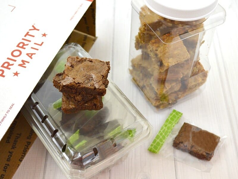 Cut brownie squares stacked in an airtight container lined with parchment paper on a kitchen counter