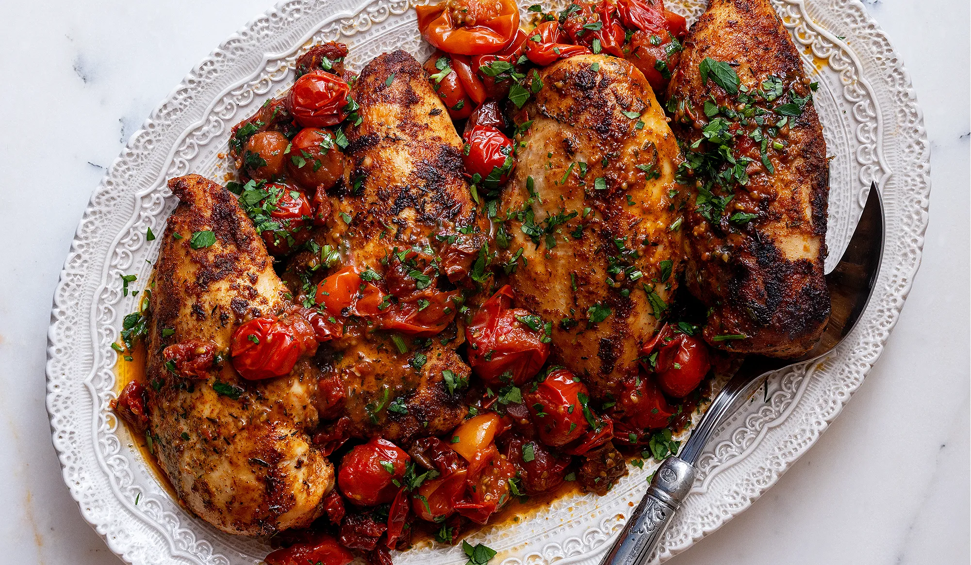 Cut chicken pieces, minced garlic, and sliced sun-dried tomatoes ready on a cutting board next to a large skillet on the stove