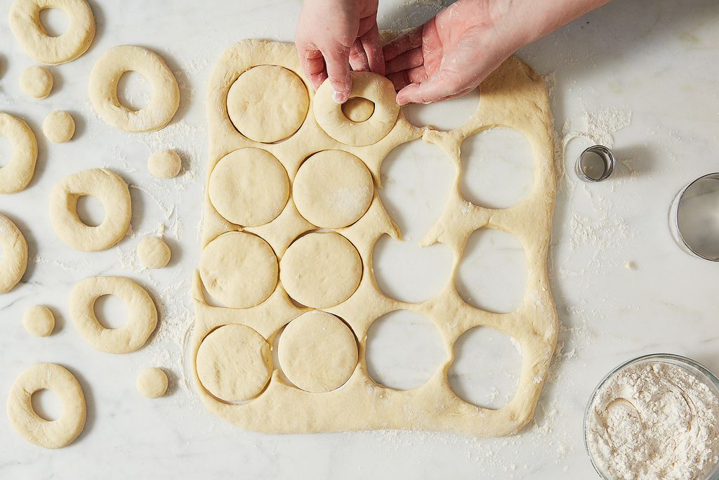 Cut donut rings and donut holes resting on parchment paper on a sheet pan
