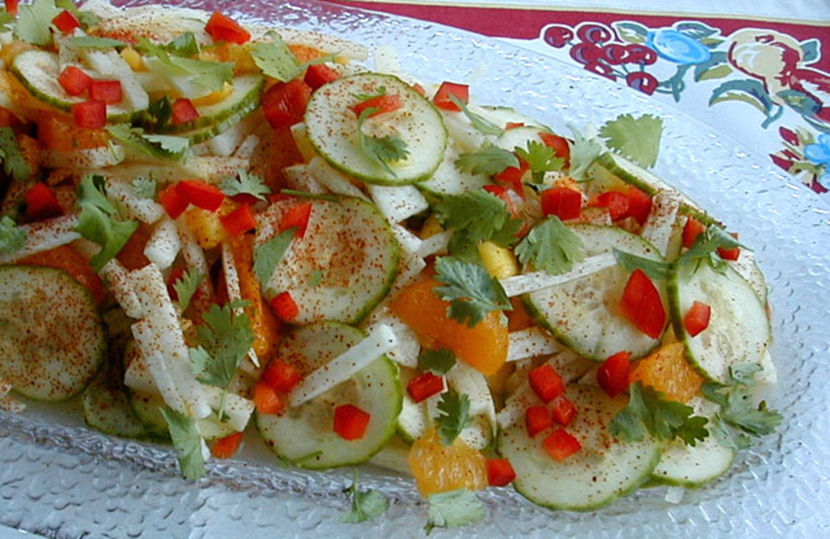 Cut jicama sticks with sliced cucumber, diced mango, thinly sliced red onion, and chopped cilantro on a cutting board