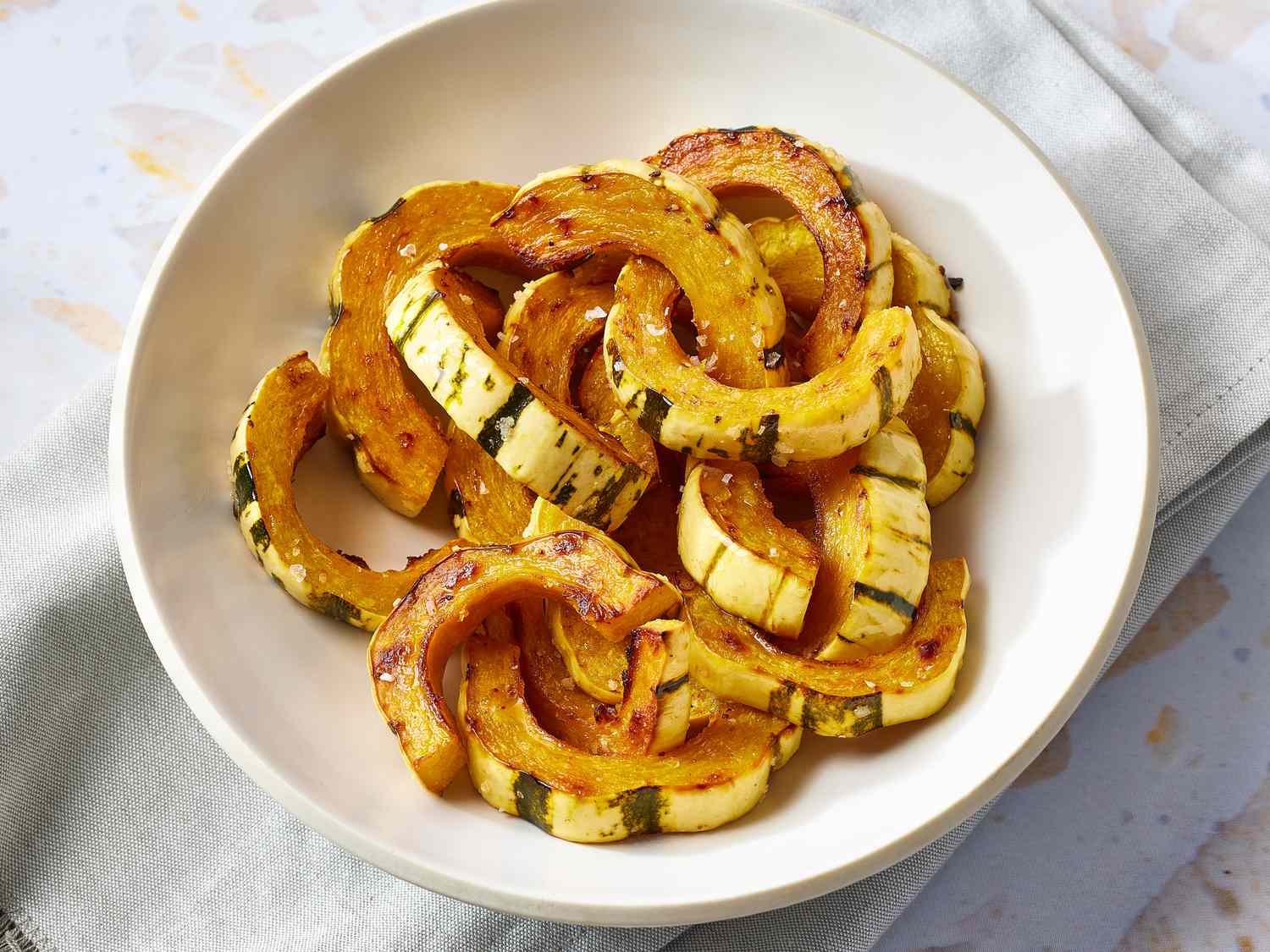 Delicata squash, butter, fresh sage, maple syrup, salt, pepper, and red pepper flakes arranged on a tidy kitchen counter with warm natural light