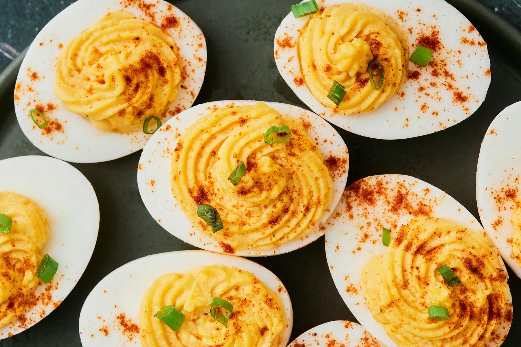Deviled eggs topped with paprika and chopped chives arranged on a serving platter