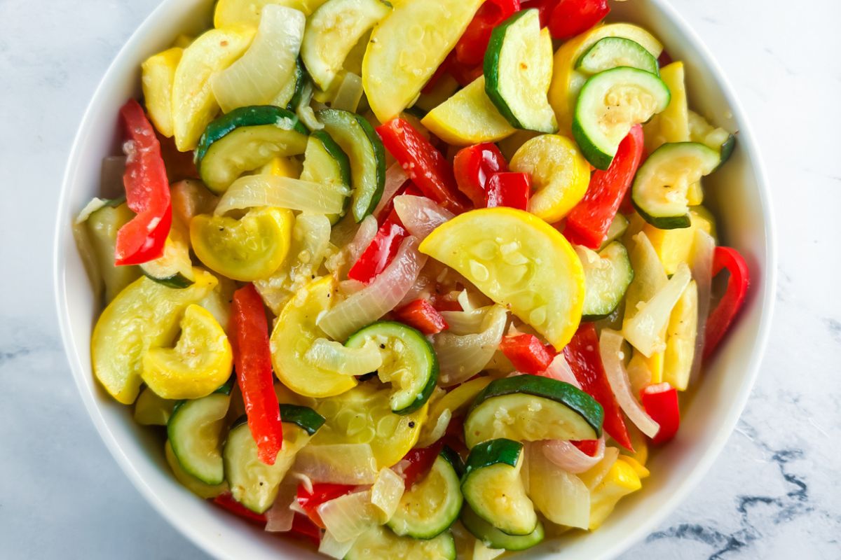 Diced bell pepper, diced onion, chopped zucchini, garlic, and small bowls of spices arranged on a kitchen counter beside a skillet