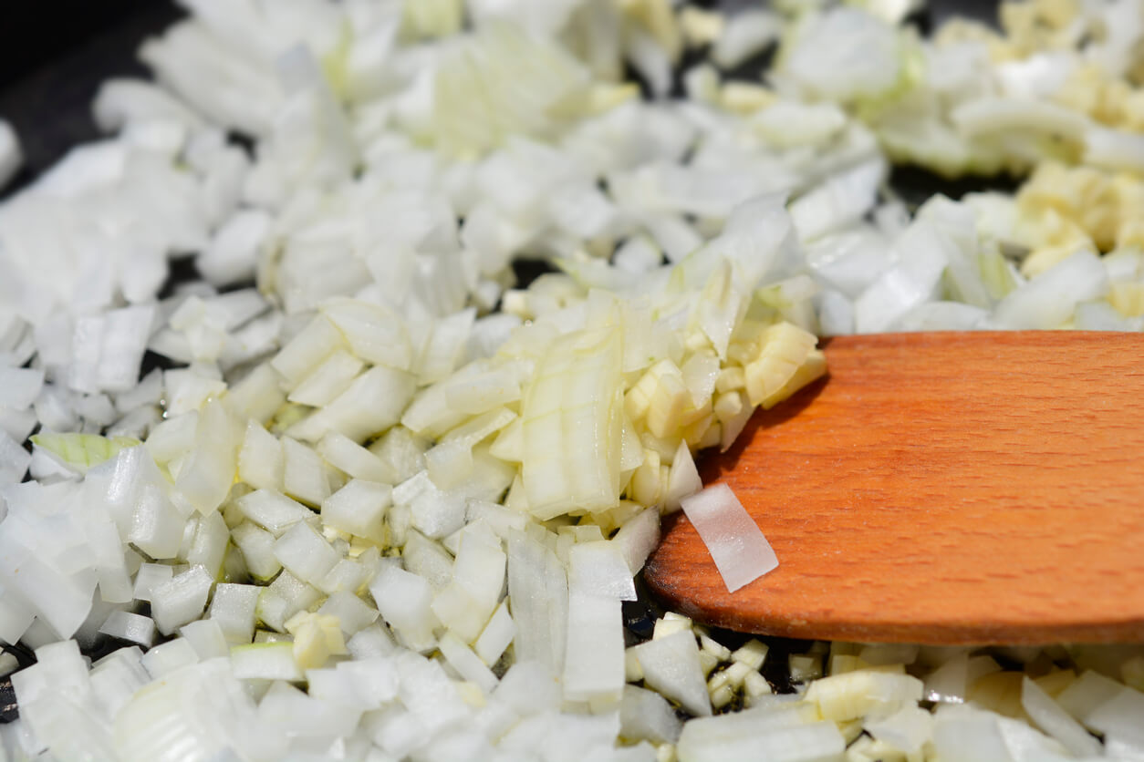 Diced onion and minced garlic on a cutting board next to a skillet warming on the stove in a home kitchen