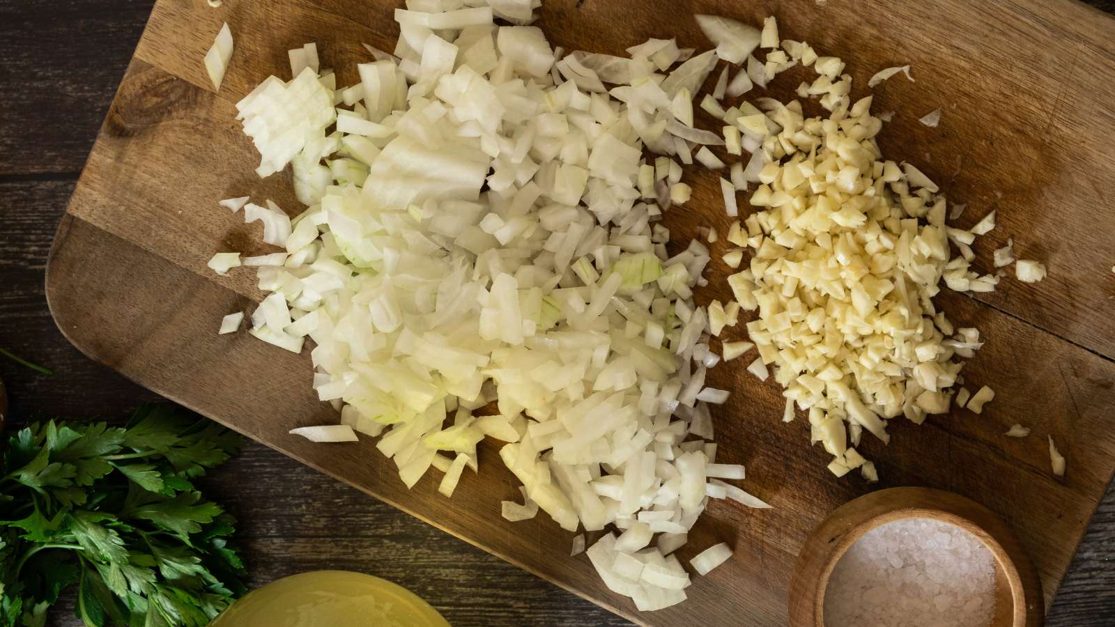 Diced onion and minced garlic on a cutting board with a chef’s knife in a home kitchen