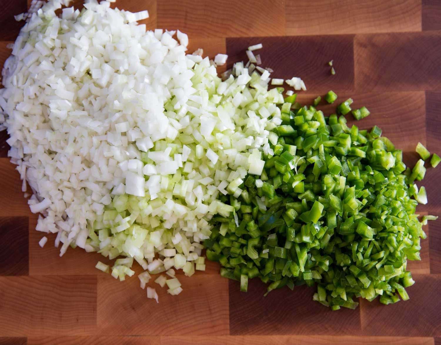 Diced onion, celery, green bell pepper, and minced garlic arranged on a cutting board on a home kitchen counter