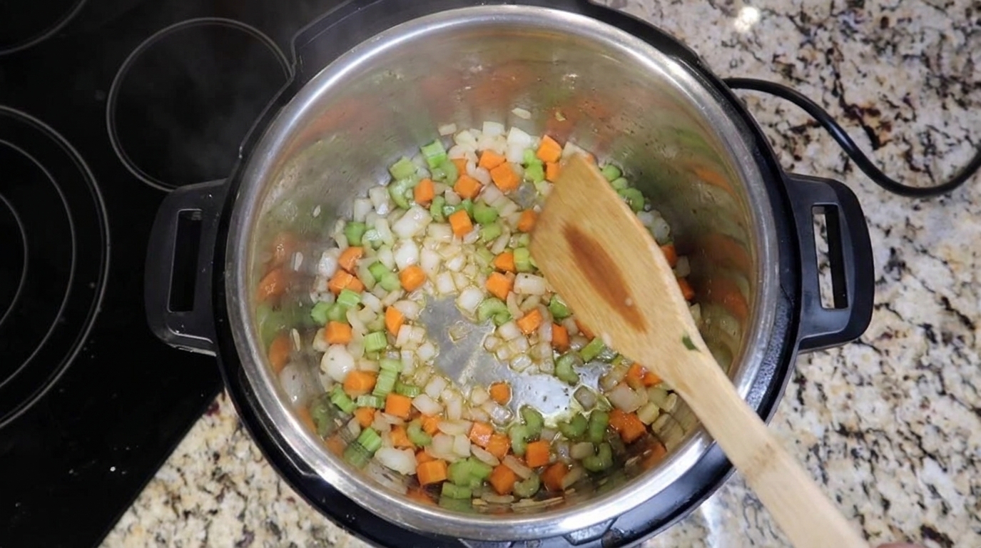 Diced onions, carrots, and celery sautéing in a large pot on the stove, glossy and lightly browned
