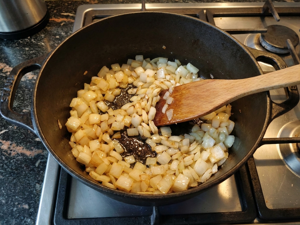 Diced onions sautéing in a heavy-bottom pot on a stovetop, turning translucent and lightly golden
