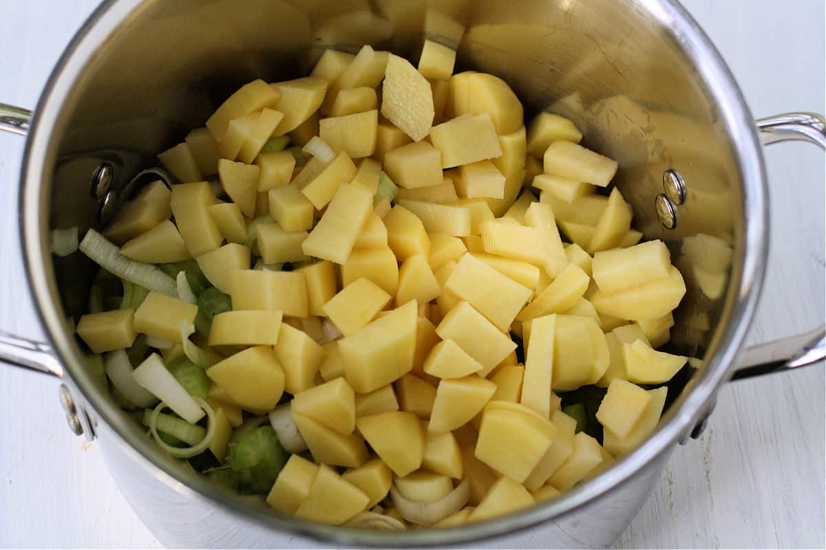 Diced potatoes, chopped onion, and sliced celery on a cutting board with a chef's knife, ready for cooking