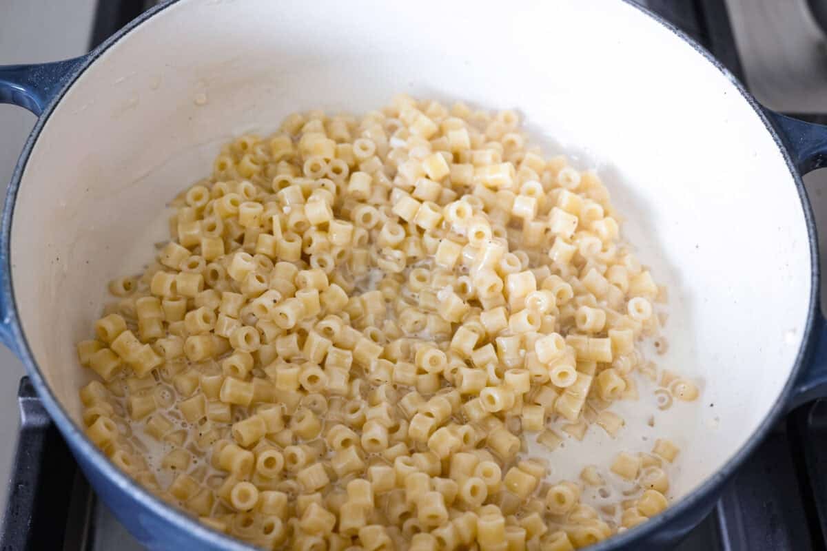 Ditalini pasta boiling in a stainless steel pot on a stovetop with gentle steam rising