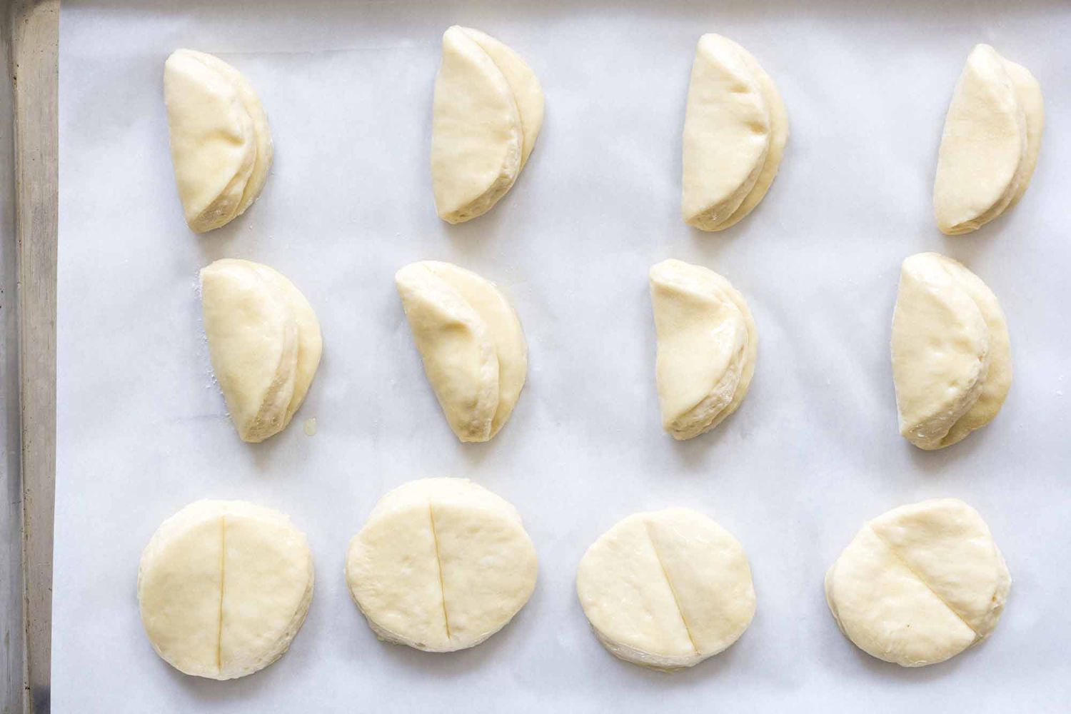Dough rectangles brushed with butter and folded with a small overhang to form the classic Parker House roll shape on a lightly floured countertop