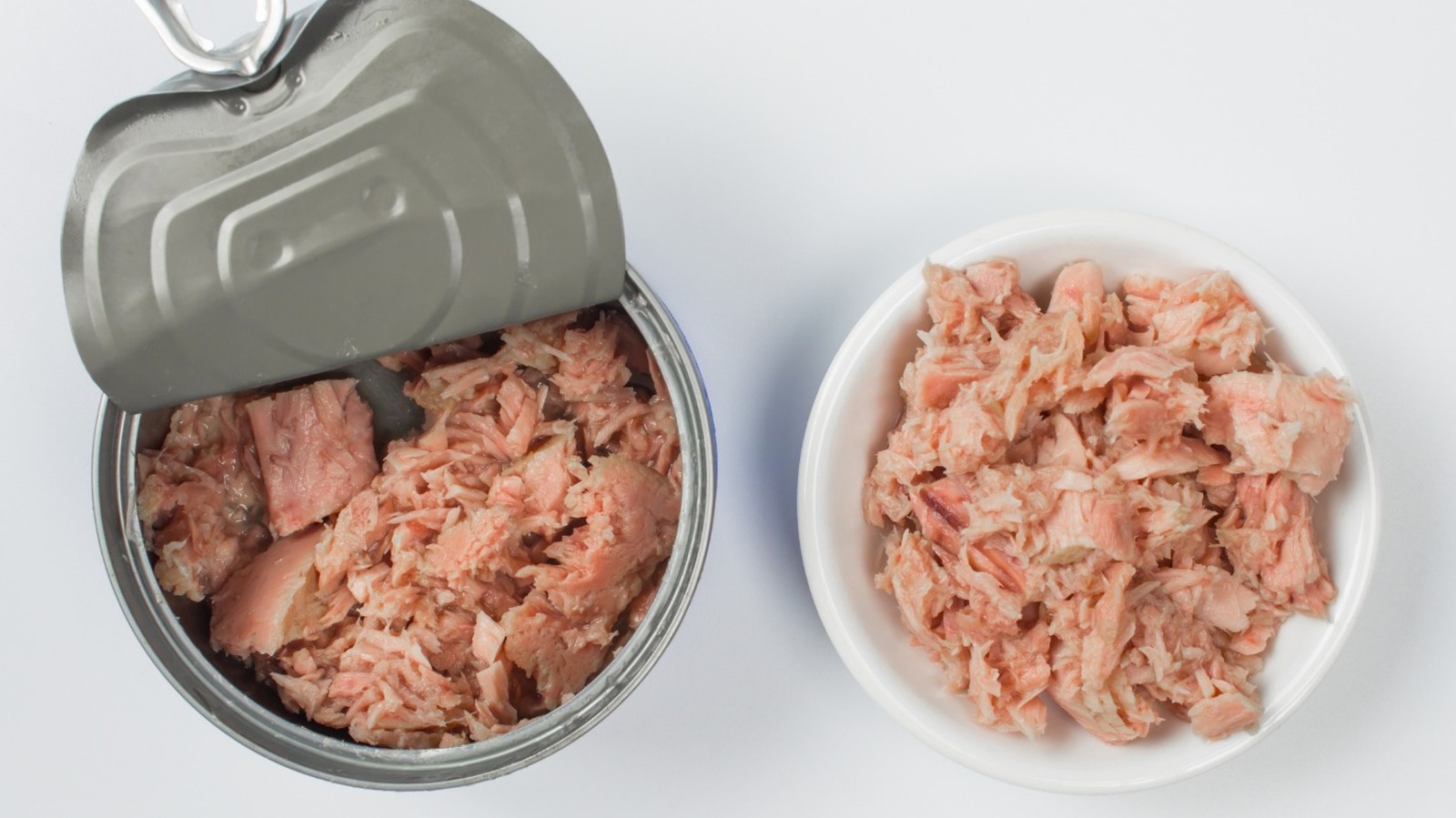 Drained tuna flakes in a glass mixing bowl with a fork resting on the rim on a bright kitchen counter