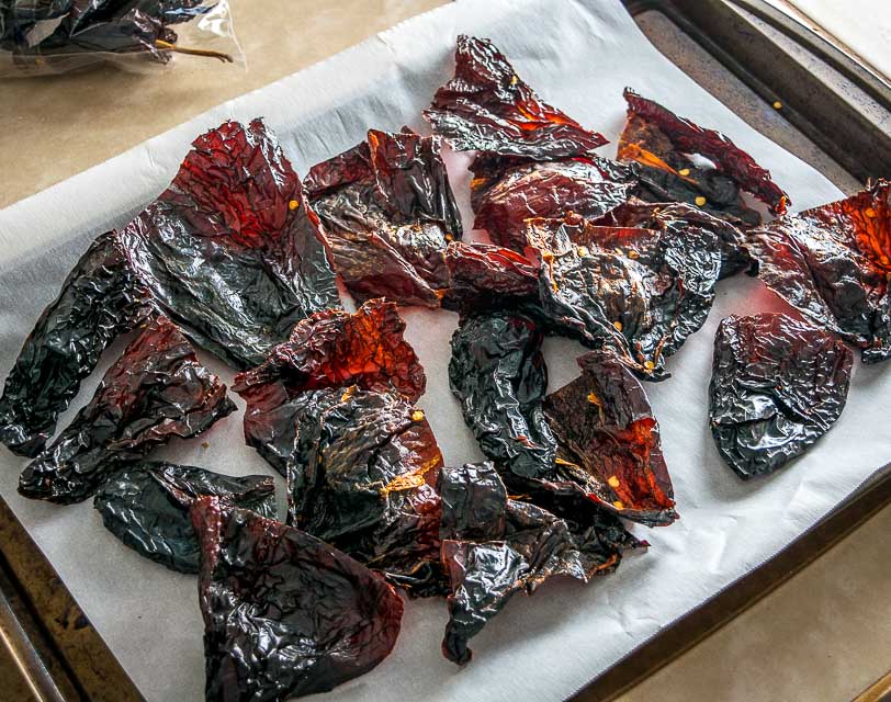 Dried ancho and pasilla chiles being lightly toasted in a hot skillet with tongs over a stovetop