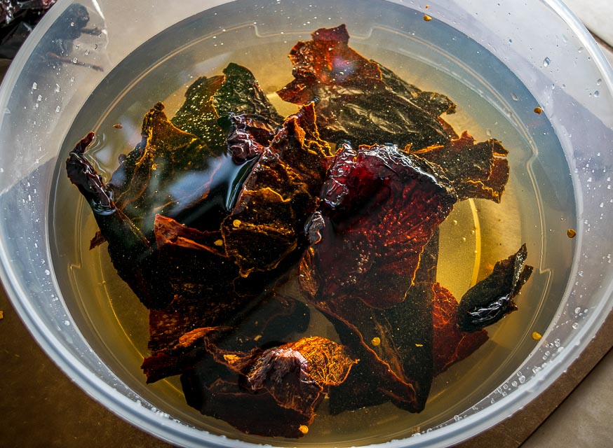 Dried chiles soaking in hot water in a glass bowl on a kitchen counter