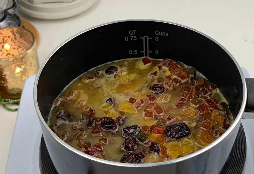 Dried fruit warming in a small saucepan with orange juice, steam rising slightly, on a clean stovetop