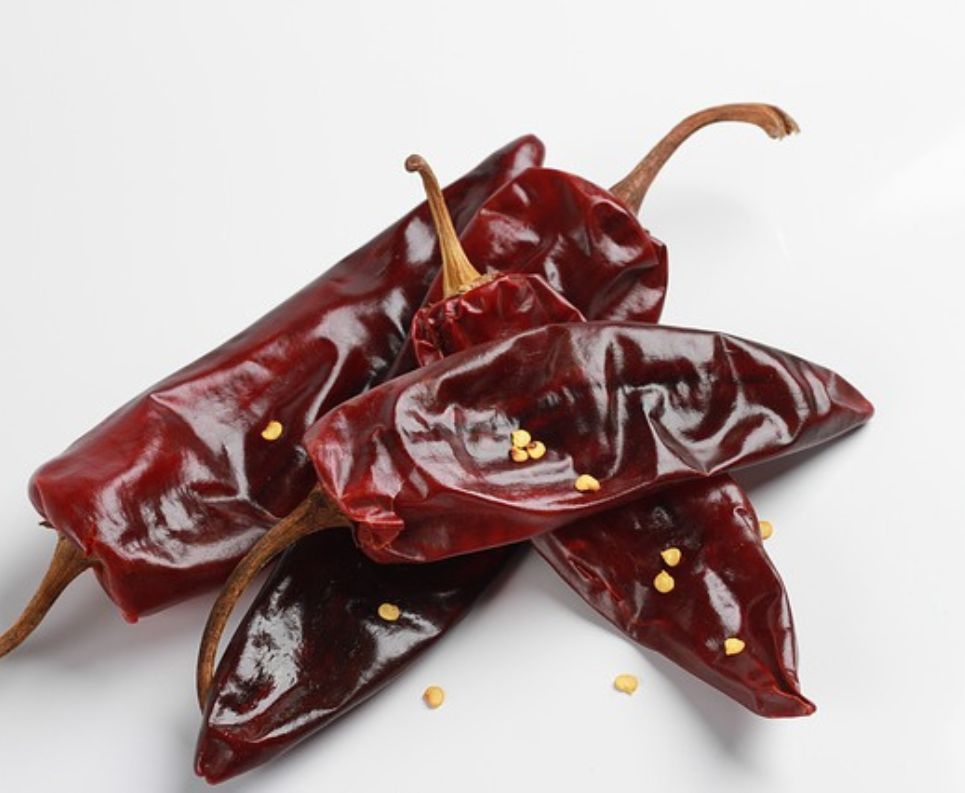 Dried guajillo and ancho chiles on a cutting board with garlic cloves and cumin nearby, on a kitchen counter under soft daylight