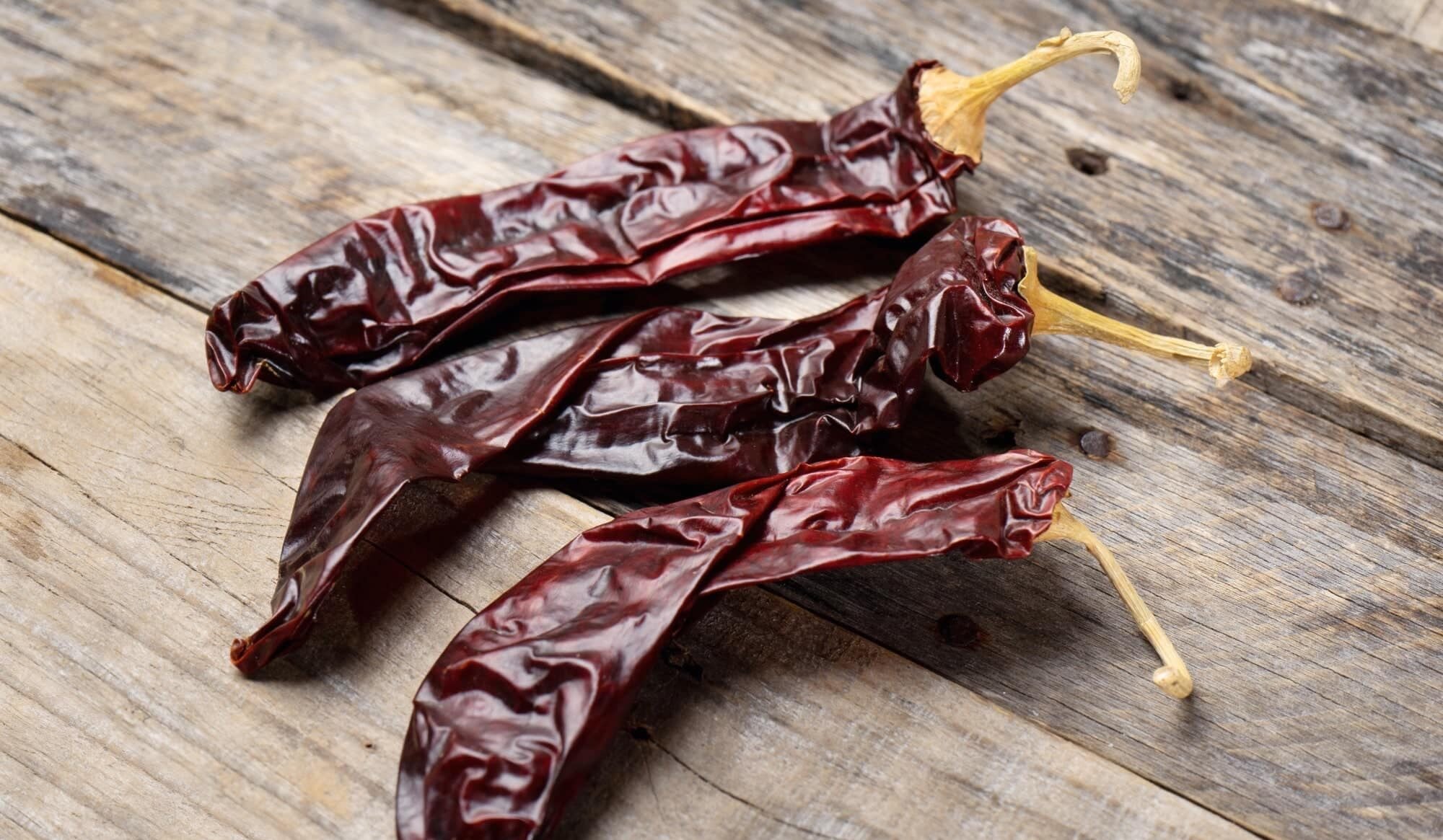 Dried guajillo and ancho chiles on a wooden cutting board on a kitchen counter