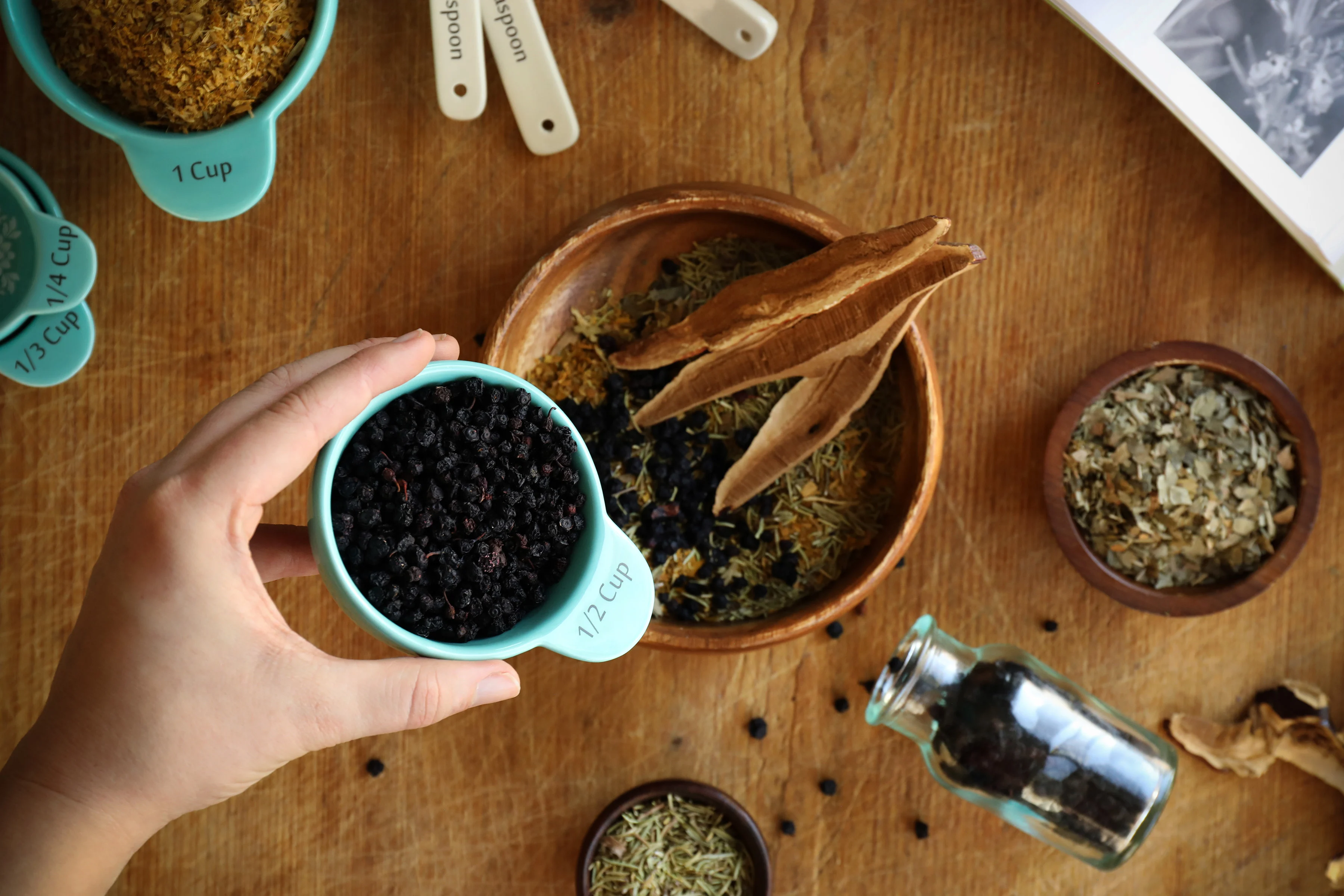 Dried sage, thyme, rosemary, and marjoram in small bowls with metal measuring spoons on a clean kitchen counter