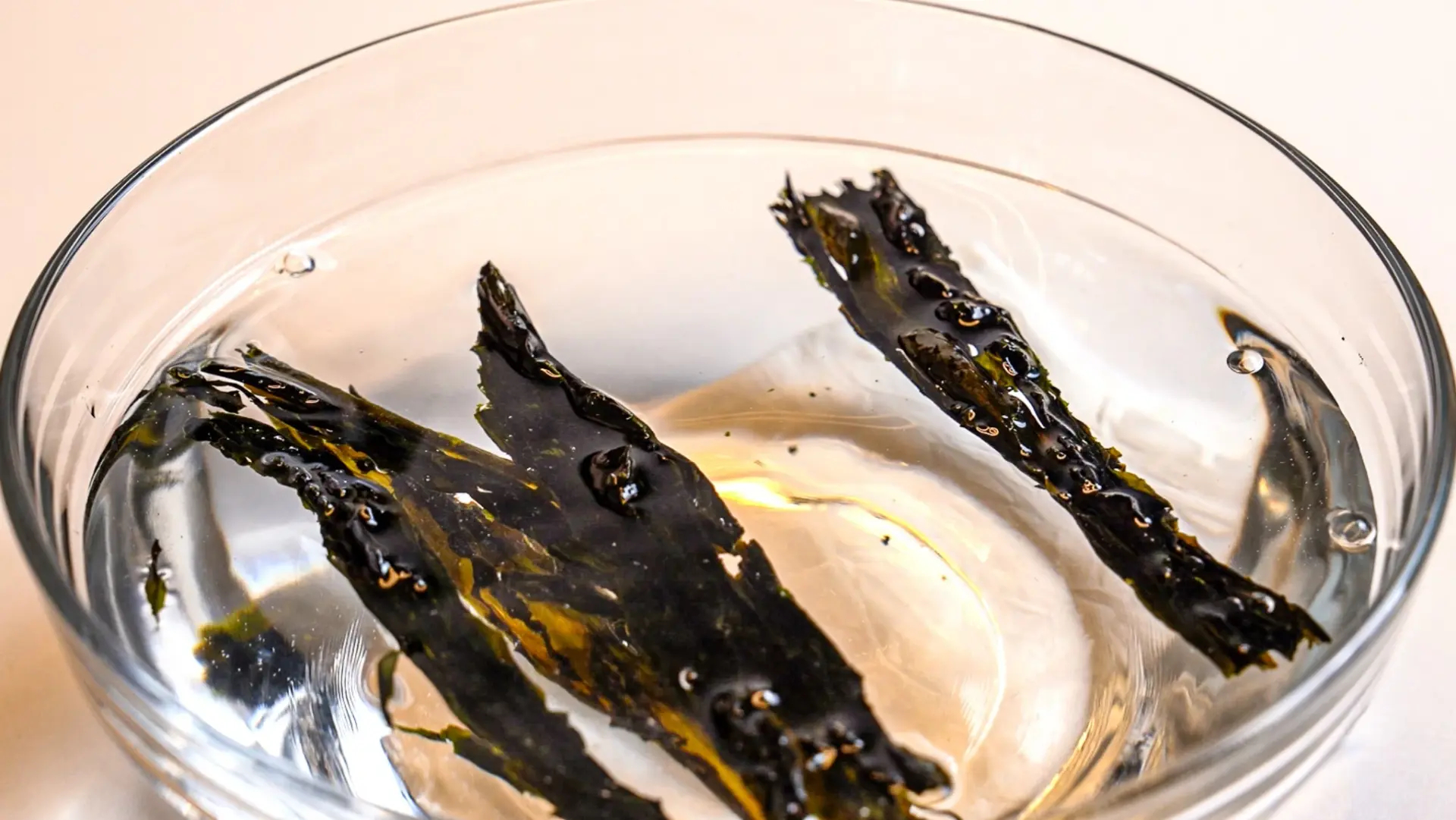 Dried wakame seaweed soaking in a small glass bowl of water on a kitchen counter