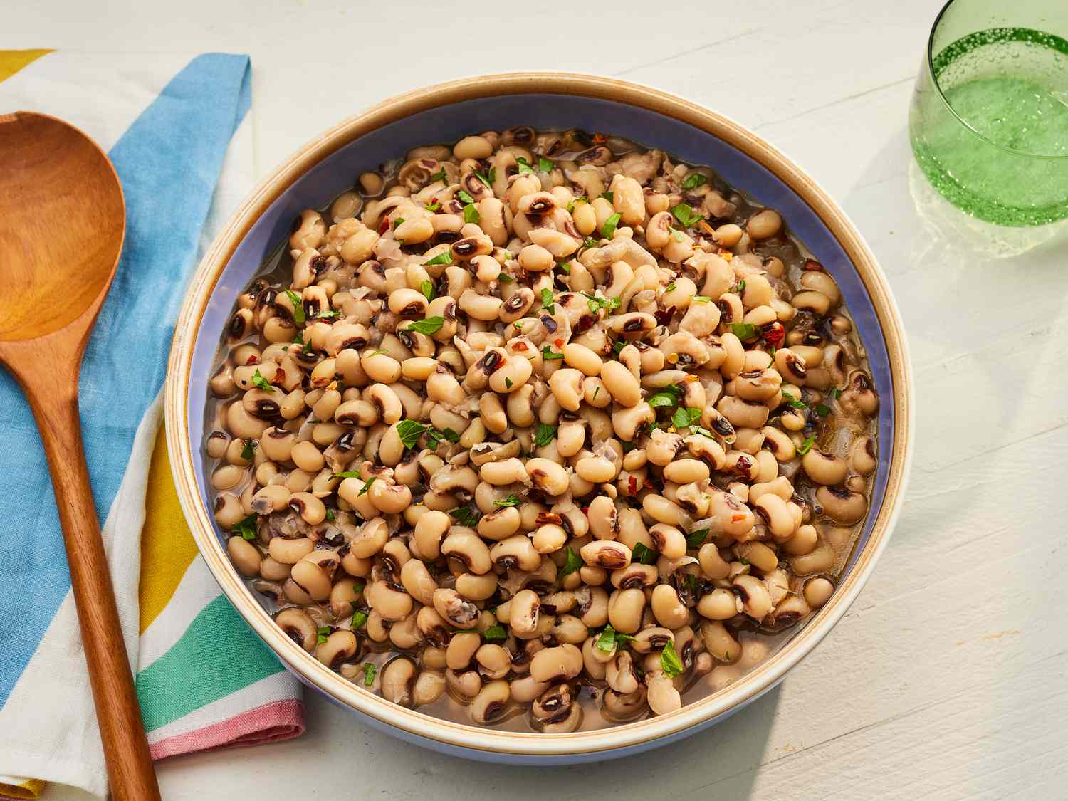 Dry black-eyed peas, bacon, onion, garlic, celery, broth, and spices arranged on a clean kitchen counter with warm overhead lighting