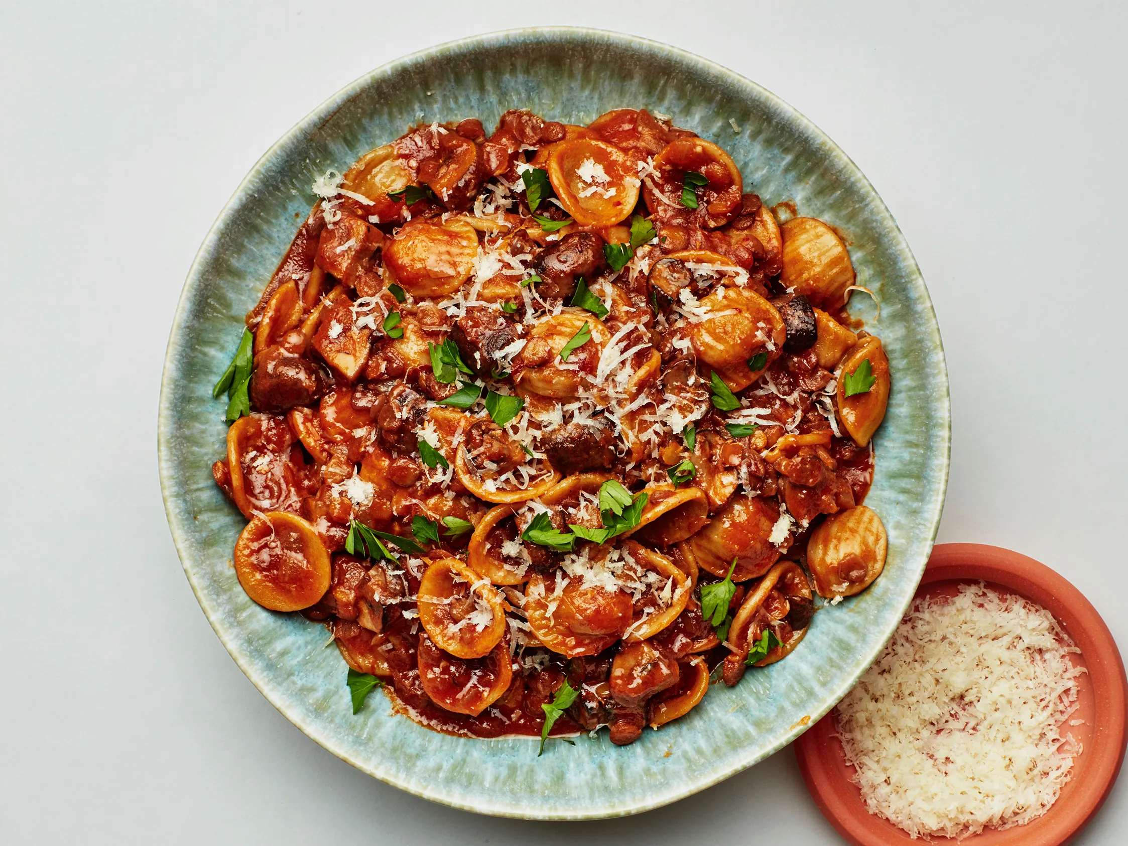 Dry brown lentils, sliced mushrooms, canned tomatoes, onion, garlic, and herbs arranged on a clean kitchen counter with a cutting board and chef’s knife