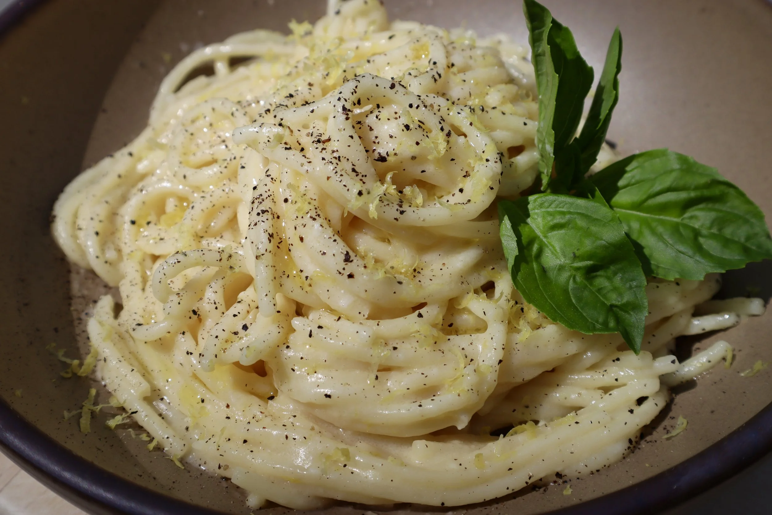 Dry spaghetti, a lemon, a stick of butter, olive oil, and a bowl of grated Parmesan arranged on a warm kitchen counter ready for cooking