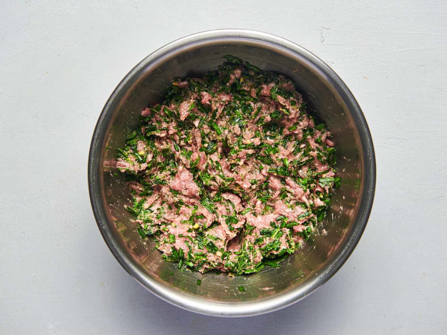 Dumpling ingredients arranged on a home kitchen counter including ground pork, napa cabbage, scallions, ginger, garlic, soy sauce, sesame oil, and round dumpling wrappers
