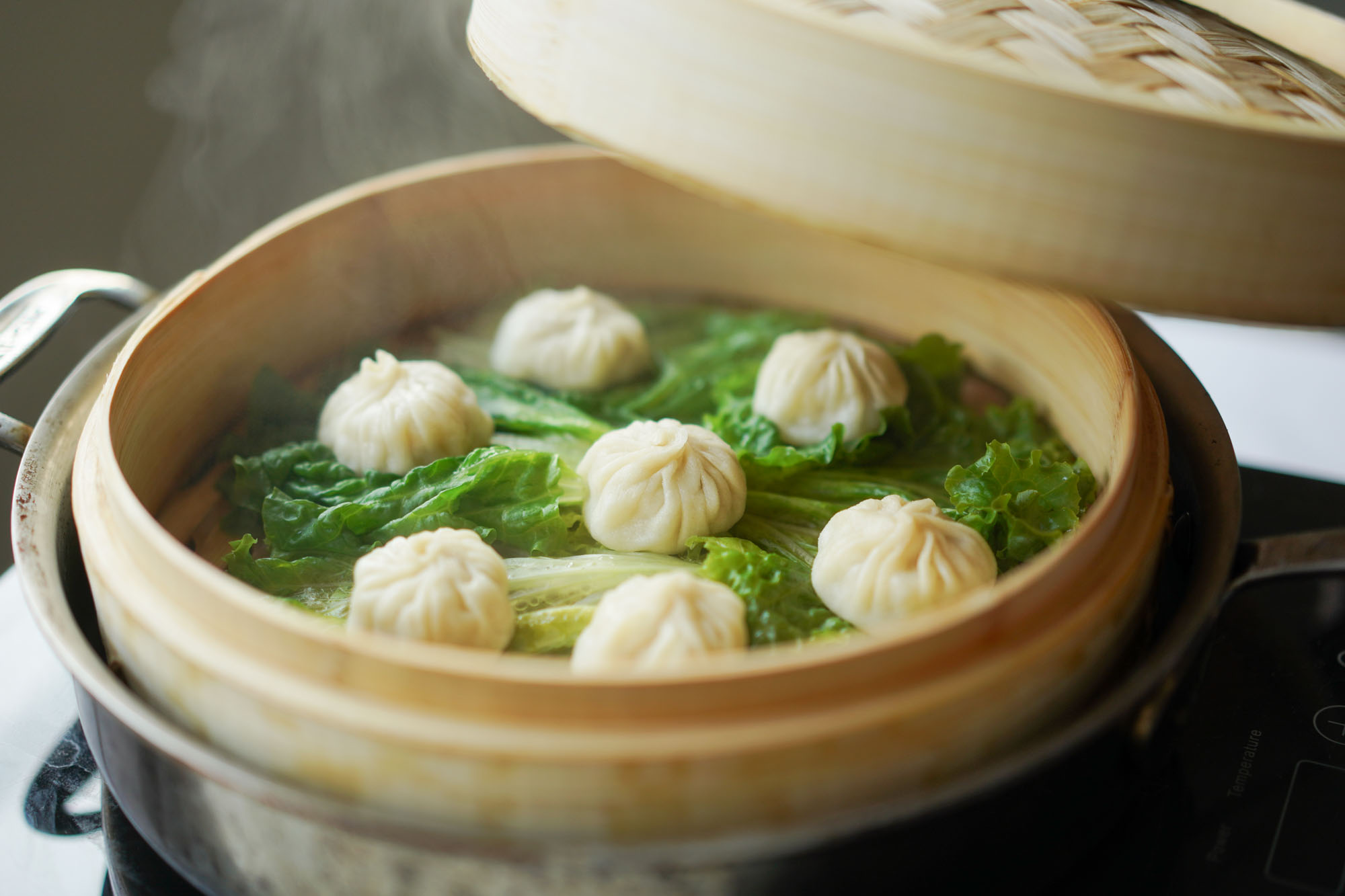 Dumpling wrappers being pleated into xiao long bao on a floured wooden board, with gathered folds meeting at the top