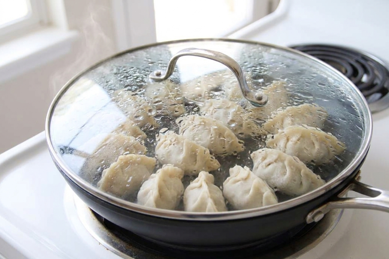 Dumplings steaming in a nonstick skillet with a lid on, condensation visible on the lid, on a home stove