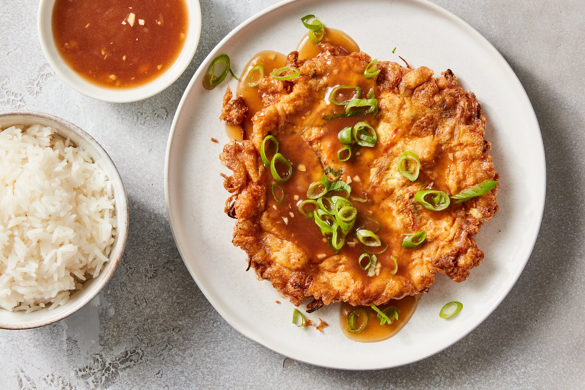 Egg foo yung patties sizzling in a nonstick skillet with visible crisping edges and a spatula ready to flip